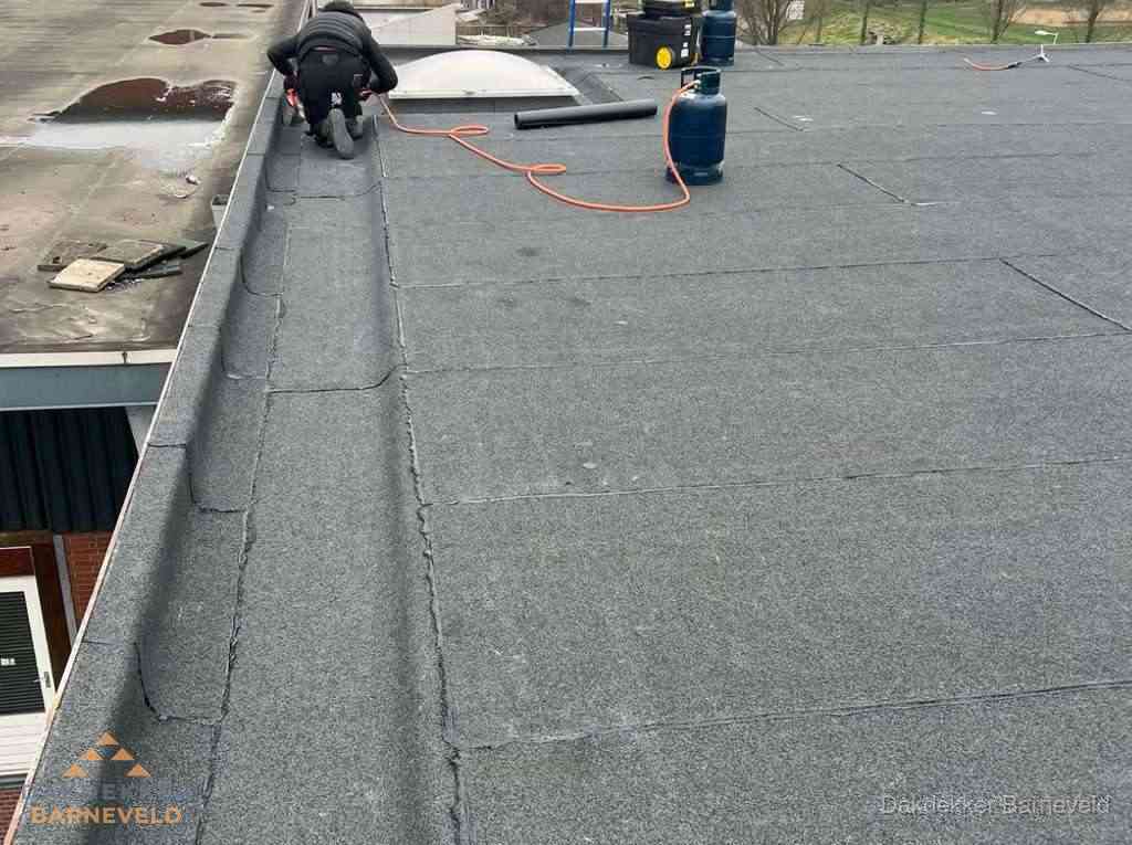 Dakdekker repareert bitumen dakbedekking op groot plat dak in Barneveld
